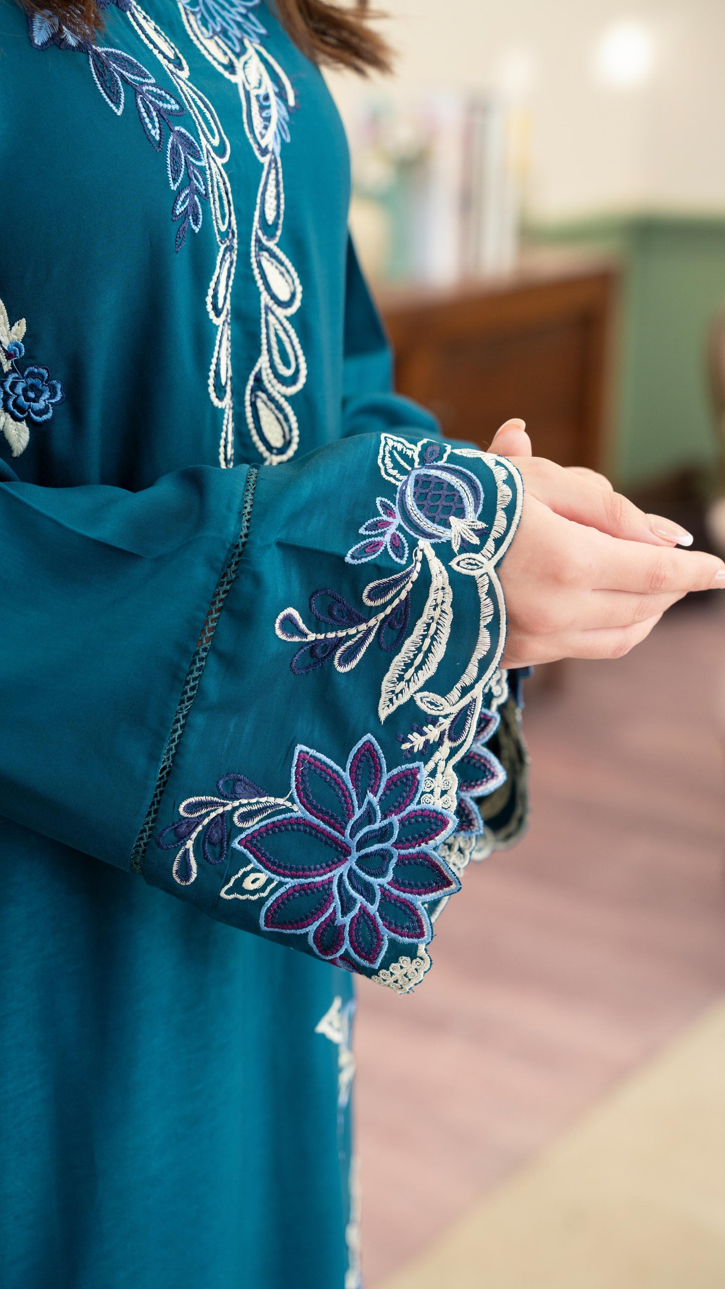 Teal dress with intricate white floral embroidery on a blurred indoor background